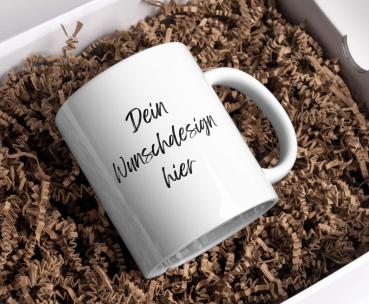 Weiße Keramiktasse in einem Geschenkbox mit der Aufschrift „Dein Wunschdesign hier“ in schwarzer Schrift. Die Tasse liegt in natürlichem, braunem Füllmaterial und ist personalisierbar – perfekt als individuelles Geschenk oder für den persönlichen Gebrauch